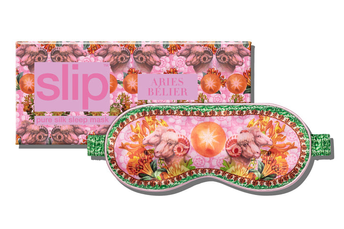 A silk sleep mask with a floral and celestial pattern, predominantly pink, green, and yellow, presented in front of its slip packaging.