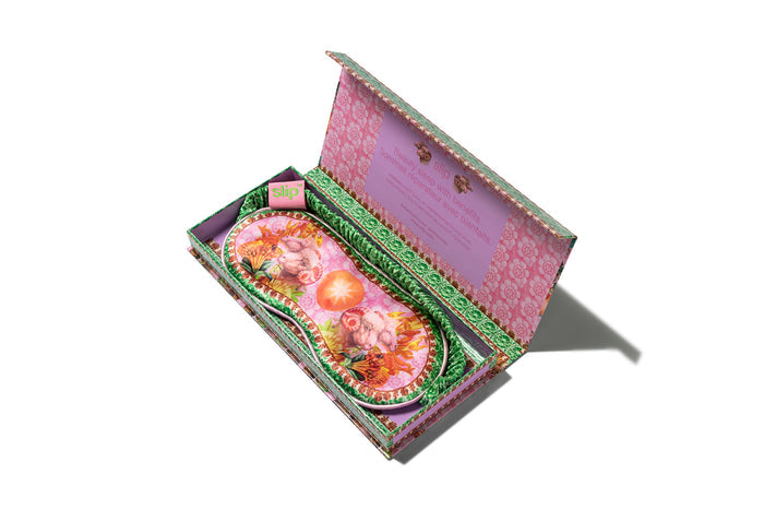 A colorful slip silk sleep mask with a zodiac Aries design, featuring pink and green tones. Displayed in branded open packaging box on white background.