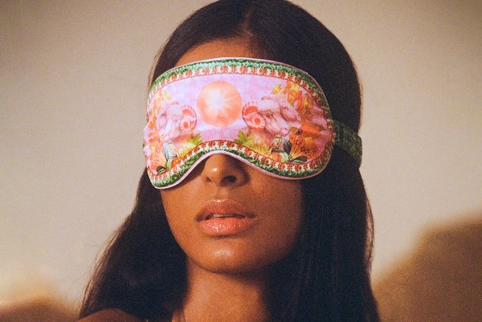 A woman wearing a colorful slip silk sleep mask with a zodiac Aries design.