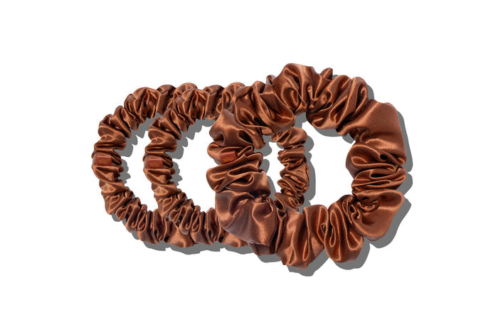 A set of three auburn slipsilk scrunchies, including two midi and one large, on a white background.