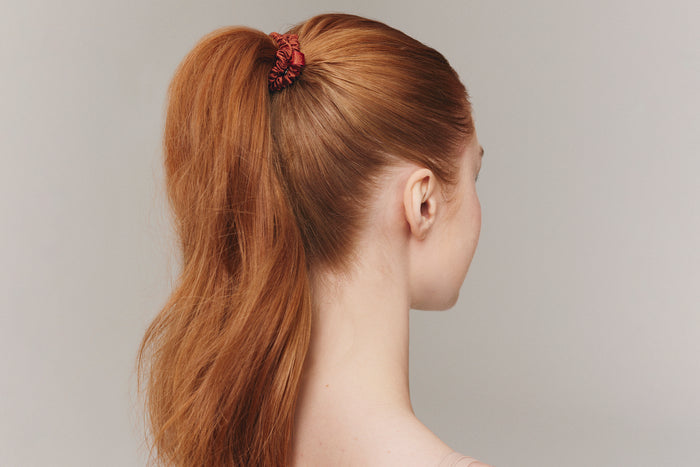 A woman wearing an auburn slip silk skinny scrunchie in her hair.