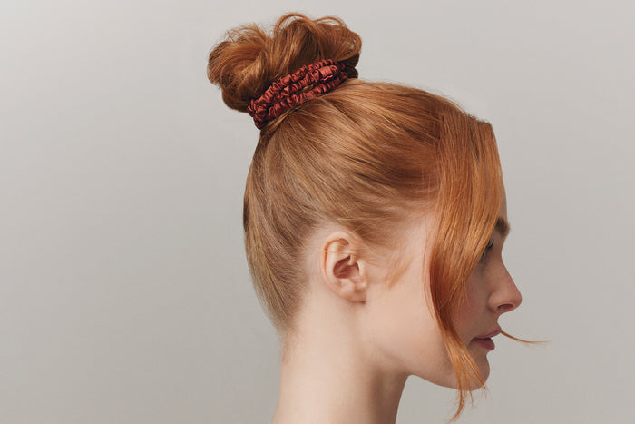 A woman wearing an auburn slip silk skinny scrunchie in her hair.