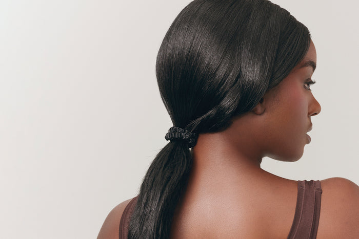 A woman wearing a black slip silk skinny scrunchie in her hair.