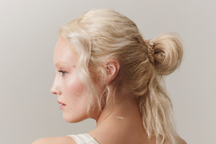 A woman wearing a blonde slip silk skinny scrunchie in her hair.