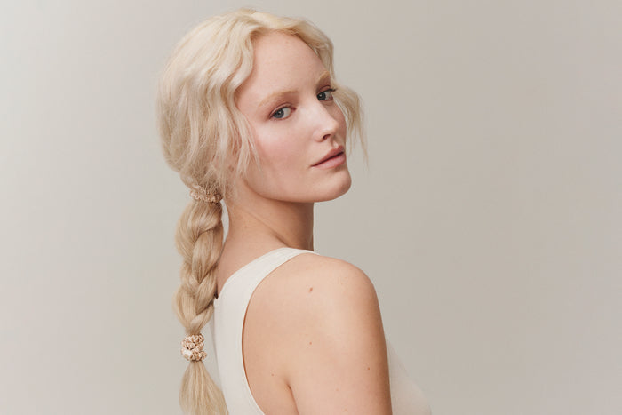 A woman with a styled plat ponytail with slip silk blonde skinny scrunchies in her hair.