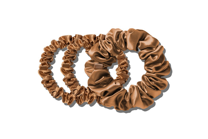 A set of three copper slipsilk scrunchies, including two midi and one large, on a white background.