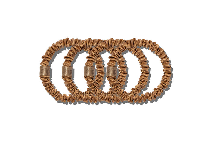 A set of four slip silk copper skinny scrunchies on a white background.