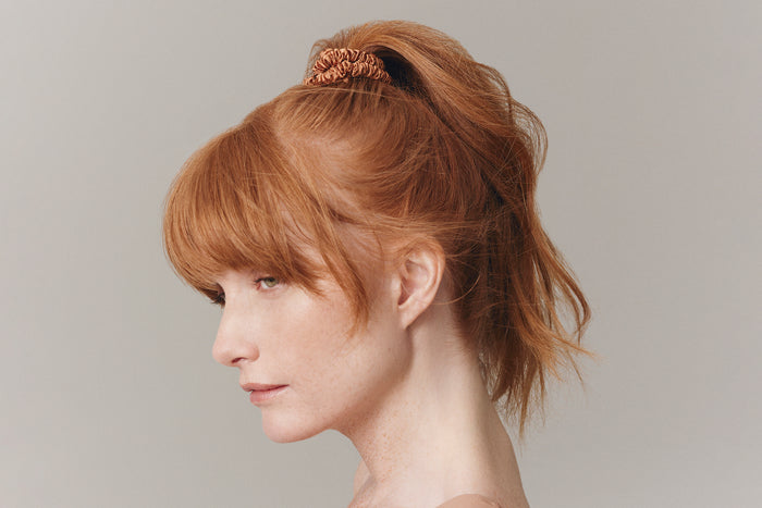 A woman wearing a copper slip silk skinny scrunchie in her hair.