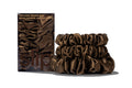 A set of three dark brown colored slipsilk scrunchies, including two midi and one large, stacked in front of branded packaging on a white background.