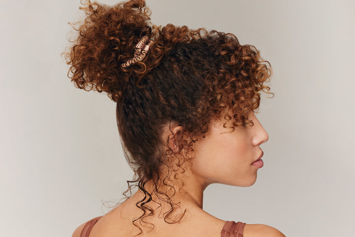 A woman wearing a light brown slip silk skinny scrunchie in her hair.