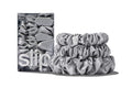 A set of three silver colored slipsilk scrunchies, including two midi and one large, stacked in front of branded packaging on a white background.