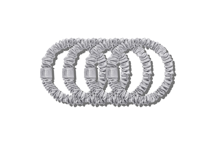 A set of four silver slip silk skinny scrunchies on a white background.