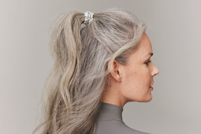 A woman wearing a silver slip silk skinny scrunchie in her hair.