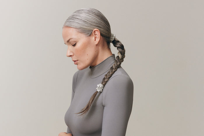 A woman with a styled plat ponytail with slip silk silver skinny scrunchies in her hair.