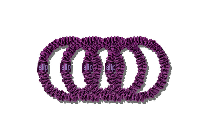 Set of four purple slip skinny silk scrunchies on a white background