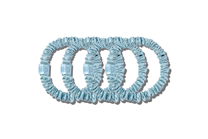 Four sky blue silk skinny scrunchies on a white background