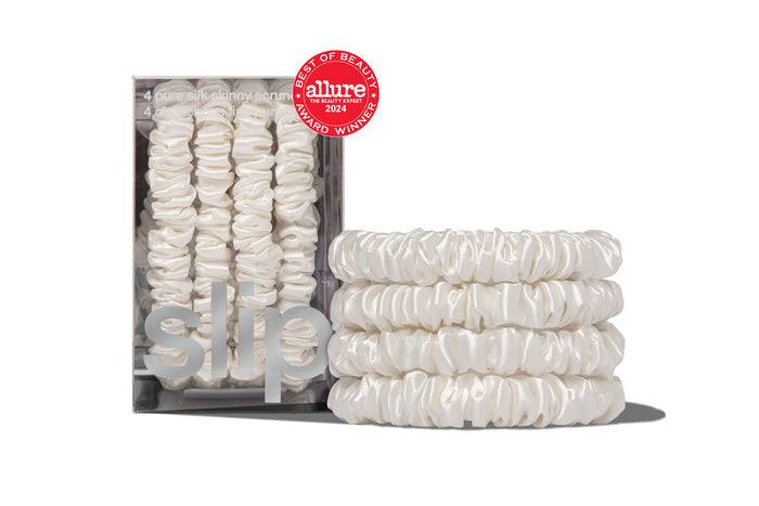 A set of four white silk skinny scrunchies displayed in a box and stacked in front with a allure award badge on a white background