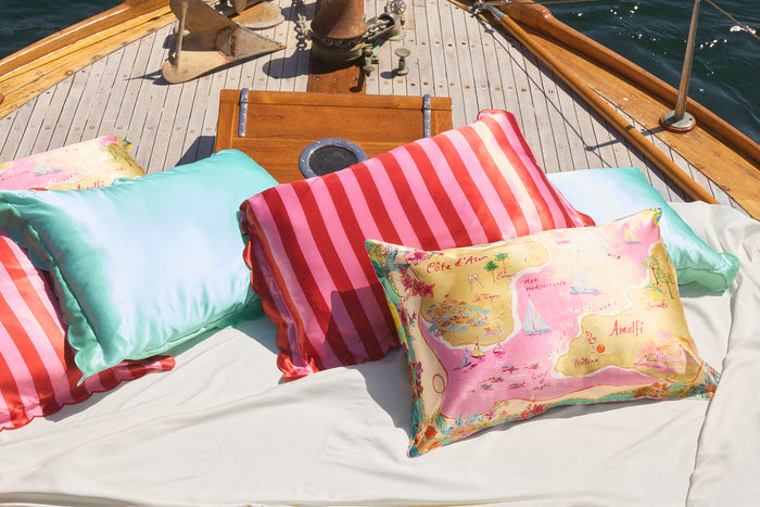Slip silk pillowcases in turquoise, red and pink stripe and colourful map graphic, scattered on a boat.