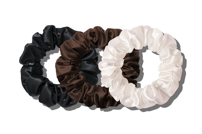 Three slip silk large hair scrunchies in black, chocolate, and white, arranged overlapping on a clean white background.
