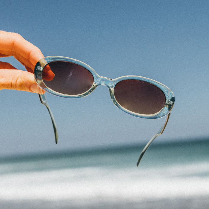 Sunglasses held by a hand against a clear blue sky