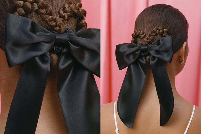 Close-up of a woman wearing a large black bow in her hair against a pink background.