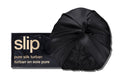 A black slip silk turban in front of with branded packaging on a white background.