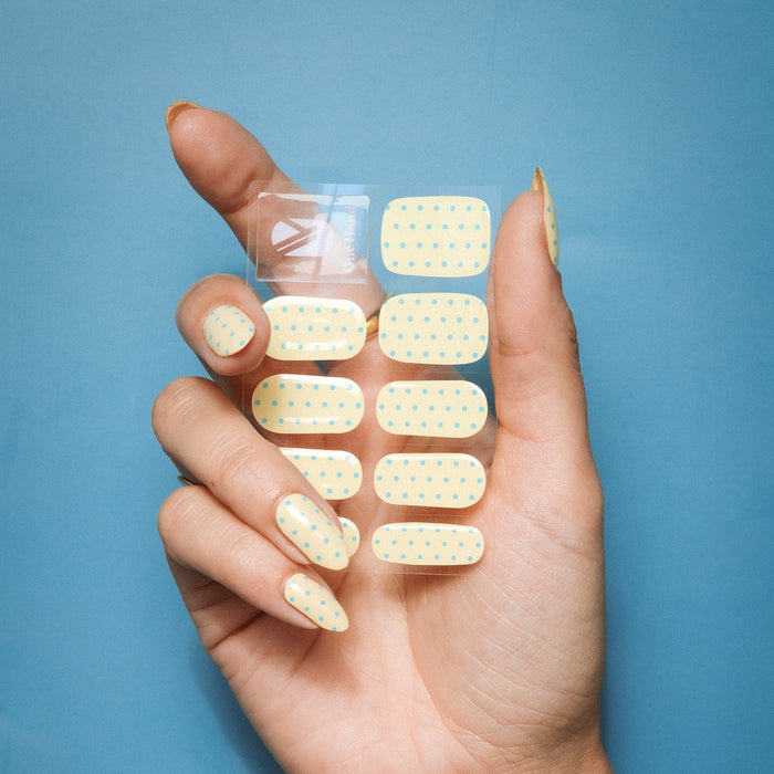 Hand holding Butter Dots gel nail sticker sheet by Maniac Nails, butter yellow nails with dots