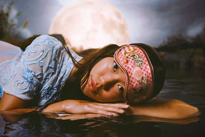 A woman wearing a floral and crab patterned slip silk sleep mask with Cancer star sign details.