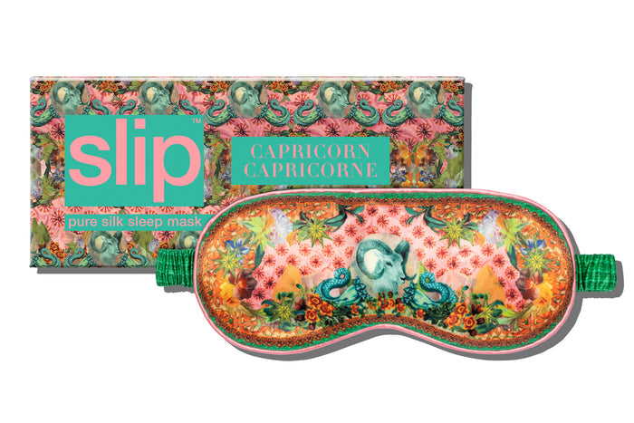 A floral patterned slip silk sleep mask with Capricorn star sign details. Displayed in front of matching branded packaging box on a white background.