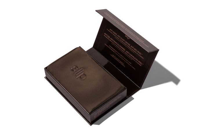A dark chocolate brown silk pillowcase box shown open on a white background, with the brand name 'slip' embroidered on the pillowcase.