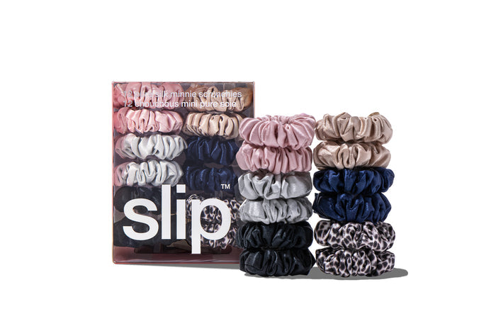 A set of twelve Slip silk minnie scrunchies in various colors including pink, caramel, silver, navy, leopard, and black, displayed in front of branded packaging on a white background.