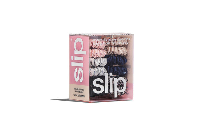 A set of twelve Slip silk minnie scrunchies in various colors including pink, caramel, silver, navy, leopard, and black in branded packaging on a white background.