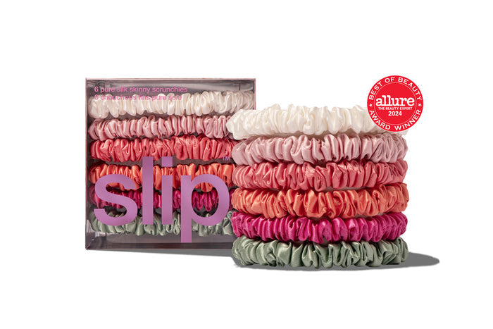 Stacks of multi-colored silk skinny scrunchies, with the brand name 'Slip' visible on the packaging.