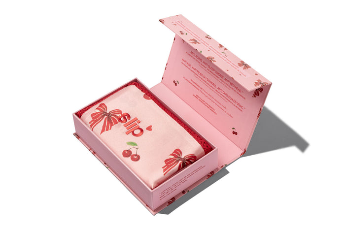 A slip silk pillowcase box with its lid open, displaying a folded pillowcase printed with red bows and cherries, set against a clean white background.