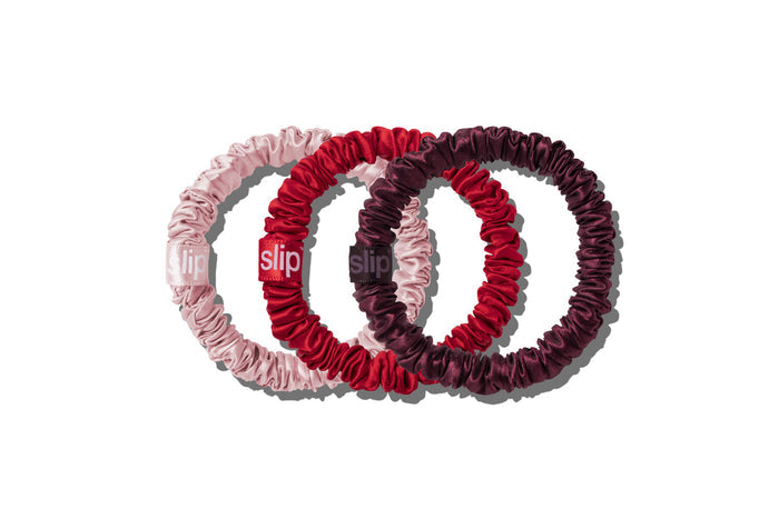 Three pure silk scrunchies in light pink, deep red, and dark burgundy, arranged in an overlapping circle on a white background.