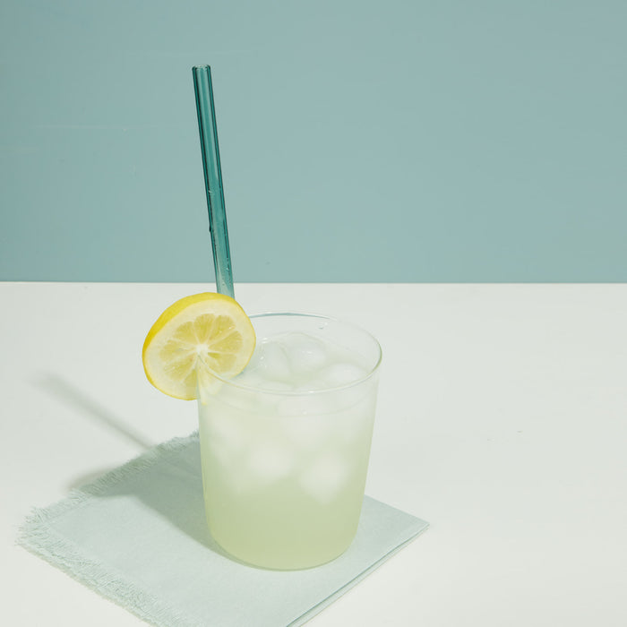 Lemonade in essential glass with straw on a light blue background.