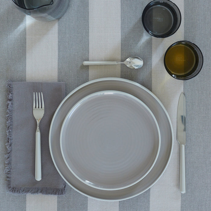 Placesetting with Essential Dinner Napkin in Dark Grey on grey striped tablecloth.