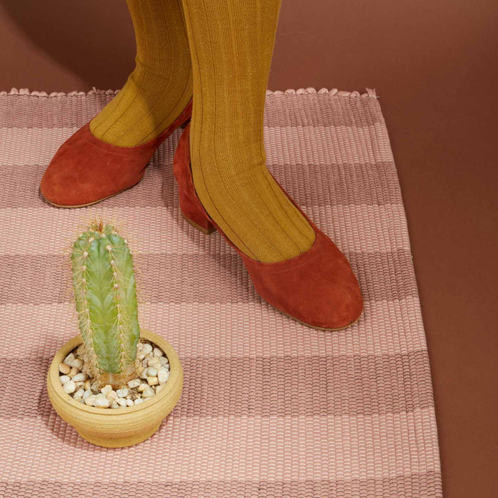 Person wearing mustard yellow socks and red shoes standing on Essential Floor Mat in Blush with a small potted cactus.