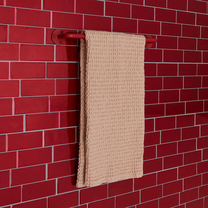 Essential towel bar in red on a tile background.