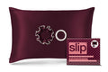 A crimson slip silk pillowcase with two scrunchies, shown next to its retail packaging box featuring the brand name 'slip'.