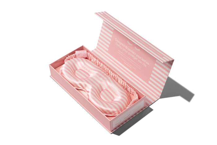 A white and pink stripe slip silk contour sleep mask, designed to protect delicate eyelash extensions. Displayed in open branded box packaging, on white background.