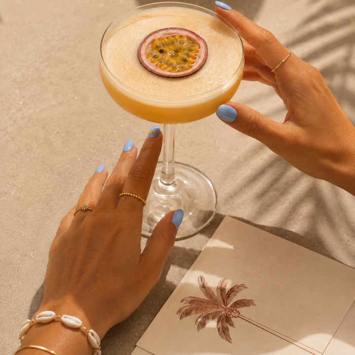 Good Vibes Only sky blue gel nail stickers by Maniac Nails, holding a passion fruit cocktail in sunlight