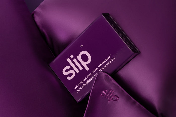 A dark purple slip silk queen pillowcase in open branded packaging resting on dark purple slip silk queen pillowcases