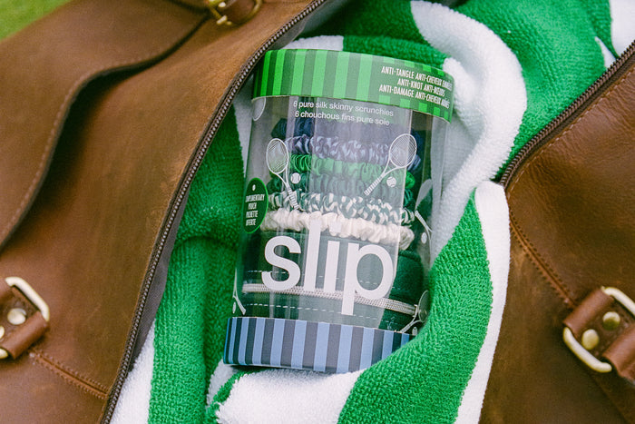 Clear slip container holding silk scrunchies with green lid inside a brown leather bag with a green towel.