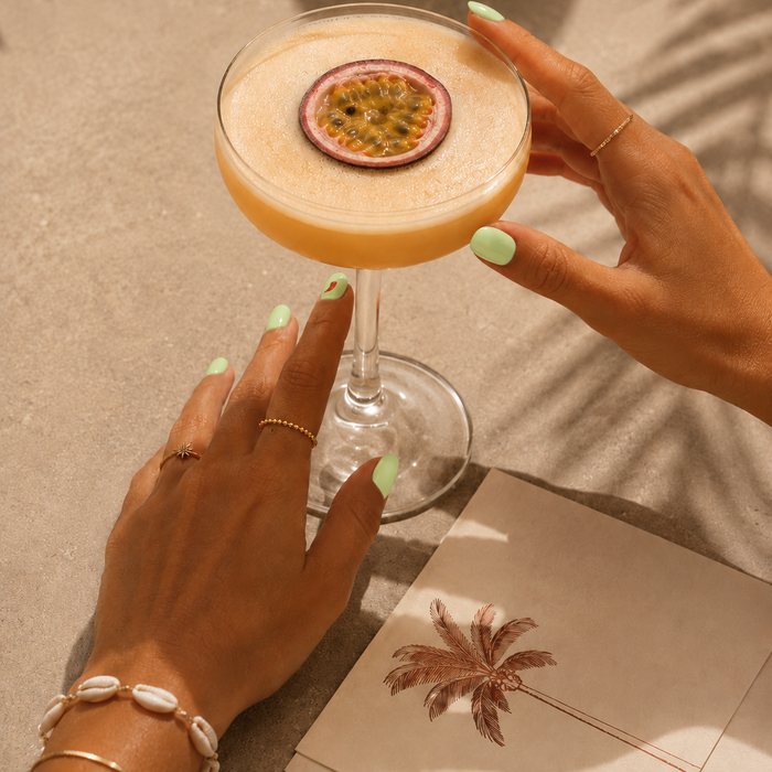 Hot & Spicy pastel green gel nail stickers by Maniac Nails, hand holding a passion fruit cocktail in golden sunlight