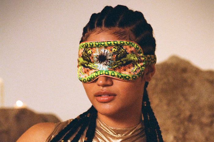 A woman wearing a colorful slip silk sleep mask with a zodiac Leo design, featuring yellow and gold tones.