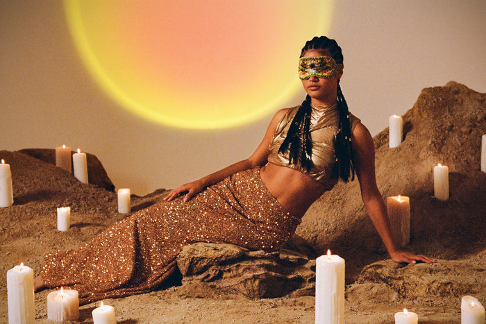 A woman wearing a colorful slip silk sleep mask with a zodiac Leo design, featuring yellow and gold tones.