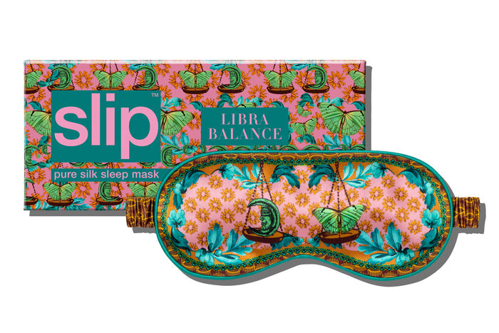 A floral pattern with scale graphic on a slip silk sleep mask for the Libra star sign. Displayed in front of branded packaging on a white background.