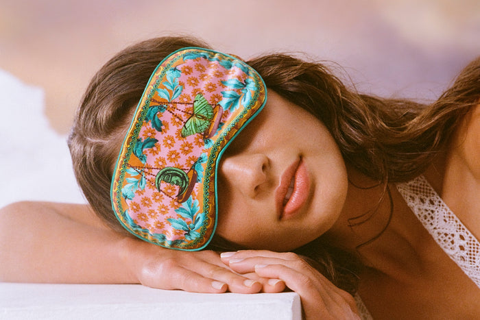 A woman wearing a floral pattern with scale graphic slip silk sleep mask for the Libra star sign.