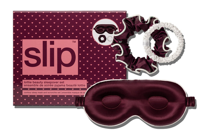 A beauty sleep set by Slip, featuring a crimson contour sleep mask, a matching scrunchie with a white trim, and a white skinny scrunchie alongside the branded packaging box on a white background.